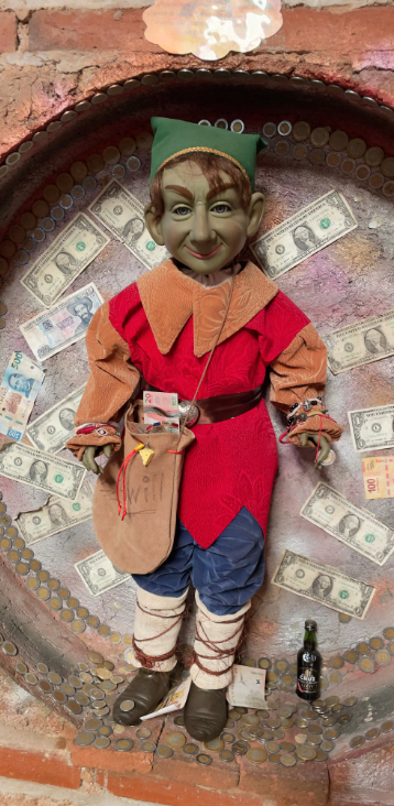 Tours Viajes gays al museo de los duendes en Hidalgo saliendo de Ciudad de México Muñeco de trapo con vestimenta colorida, ante un fondo decorado con billetes.