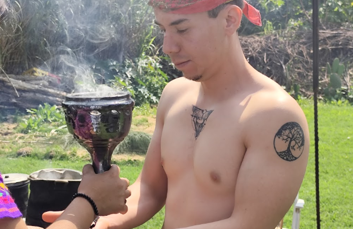 Temazcal gay en Xochimilco Joven sin camiseta sosteniendo un recipiente humeante en un entorno al aire libre.